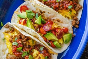 Overhead view of three breakfast tacos with chorizo on a blue oval plate.