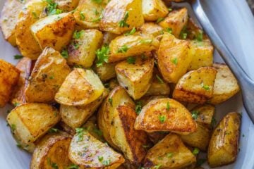 Overhead view of perfect roasted potatoes in a white serving dish, garnished with parsley.