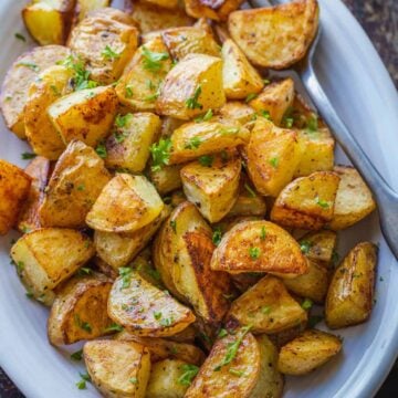 Overhead view of perfect roasted potatoes in a white serving dish, garnished with parsley.