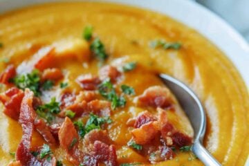 A bowl of homemade butternut squash soup garnished with bacon and parsley, with a spoon.