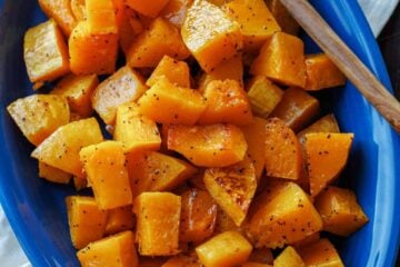 Roasted butternut squash on a blue oval platter with a serving spoon.
