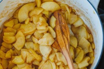 Sauteed cinnamon apples in a large pot with a wooden spoon.