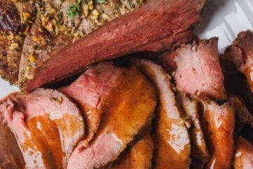 Perfect roast beef sliced thinly on a platter, drizzled with beef gravy.
