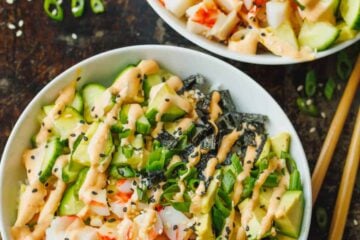 Overhead view of two California roll bowls topped with a drizzle of spicy mayo next to chopsticks.