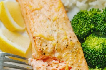 A fork flakes the end of an air fryer salmon fillet on a white plate served with broccoli and rice.