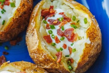 Baked potatoes on a blue plate, topped with sour cream, bacon, and chives.