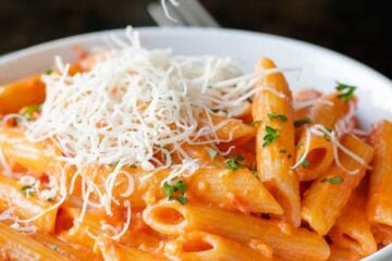 A bowl of homemade penne alla vodka topped with grated parmesan cheese and fresh herbs.