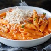 A bowl of homemade penne alla vodka topped with grated parmesan cheese and fresh herbs.