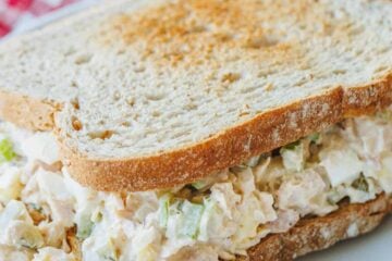 A classic tuna salad sandwich on a white plate, with a red and white checked cloth underneath.