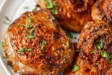 Four air fryer chicken things on a white plate garnished with freshly chopped parsley.