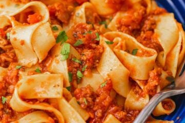 Pappardelle pasta with bolognese sauce in a blue bowl, with a fork.