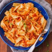 Pappardelle pasta with bolognese sauce in a blue bowl, with a fork.