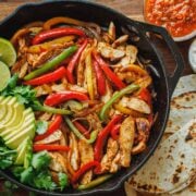 Chicken fajitas served out of a skillet with tortillas and sauces