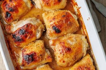 Overhead view of baked honey mustard chicken thighs in a ceramic casserole dish.