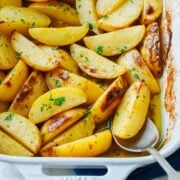 Greek lemon potato wedges in a casserole dish served with a spoon