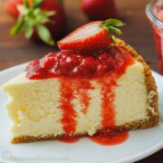 strawberry cheesecake sliced on a plate with strawberries and strawberry sauce drizzled on top