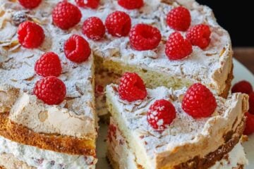 Himmelstorte layered with cake, whipped cream, and raspberries on a cake platter sliced to serve