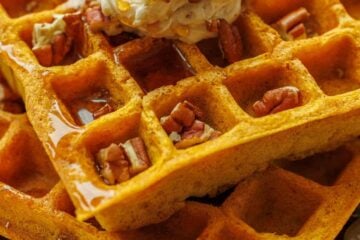 Pumpkin waffles stacked with whipped honey butter, toasted pecans, and maple syrup
