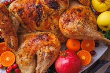Roasted spatchcocked turkey on a platter with pomegranate, oranges, and apples to garnish