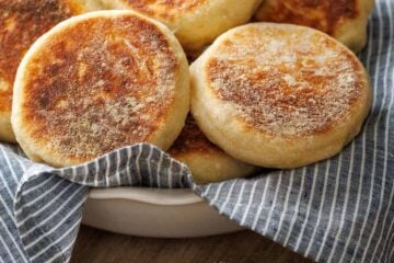 Butter spread on homemade english muffin with bowl of toasted crumpets