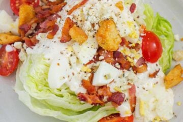Wedge salad served on a plate with dressing and toppings