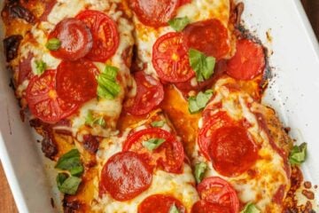 Pizza Chicken baked in a rectangle baking pan. 4 chicken breasts covered in pizza sauce, mozzarella cheese, pepperoni, and chopped basil