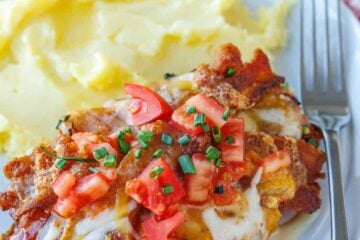 Monterey Chicken topped with melted Monterey jack cheese, tomatoes, crispy bacon, and chives. Served with mashed potatoes on a plate.