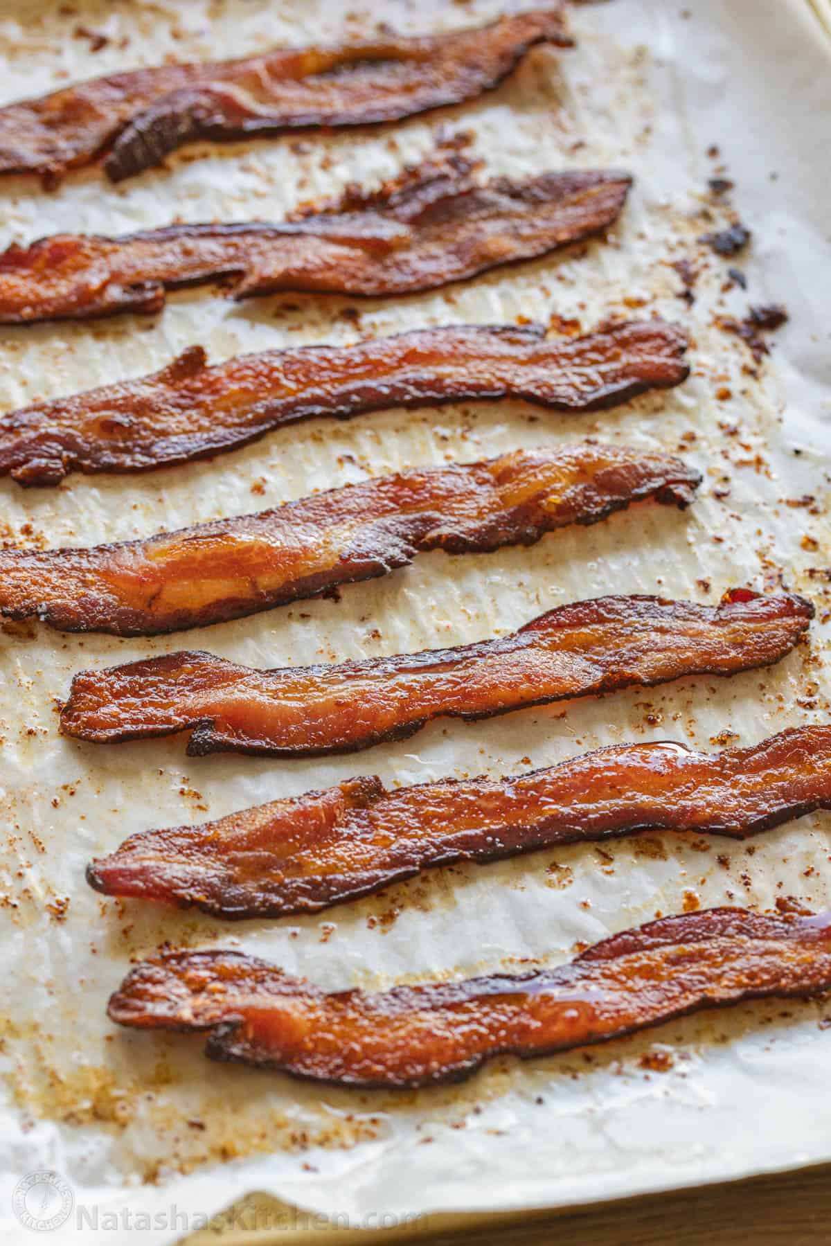 How to bake bacon in the oven that is perfectly crispy. Oven-baked bacon is the best for making a bigger batch and it's the easiest method. Crispy baked bacon on a baking sheet lined with parchment