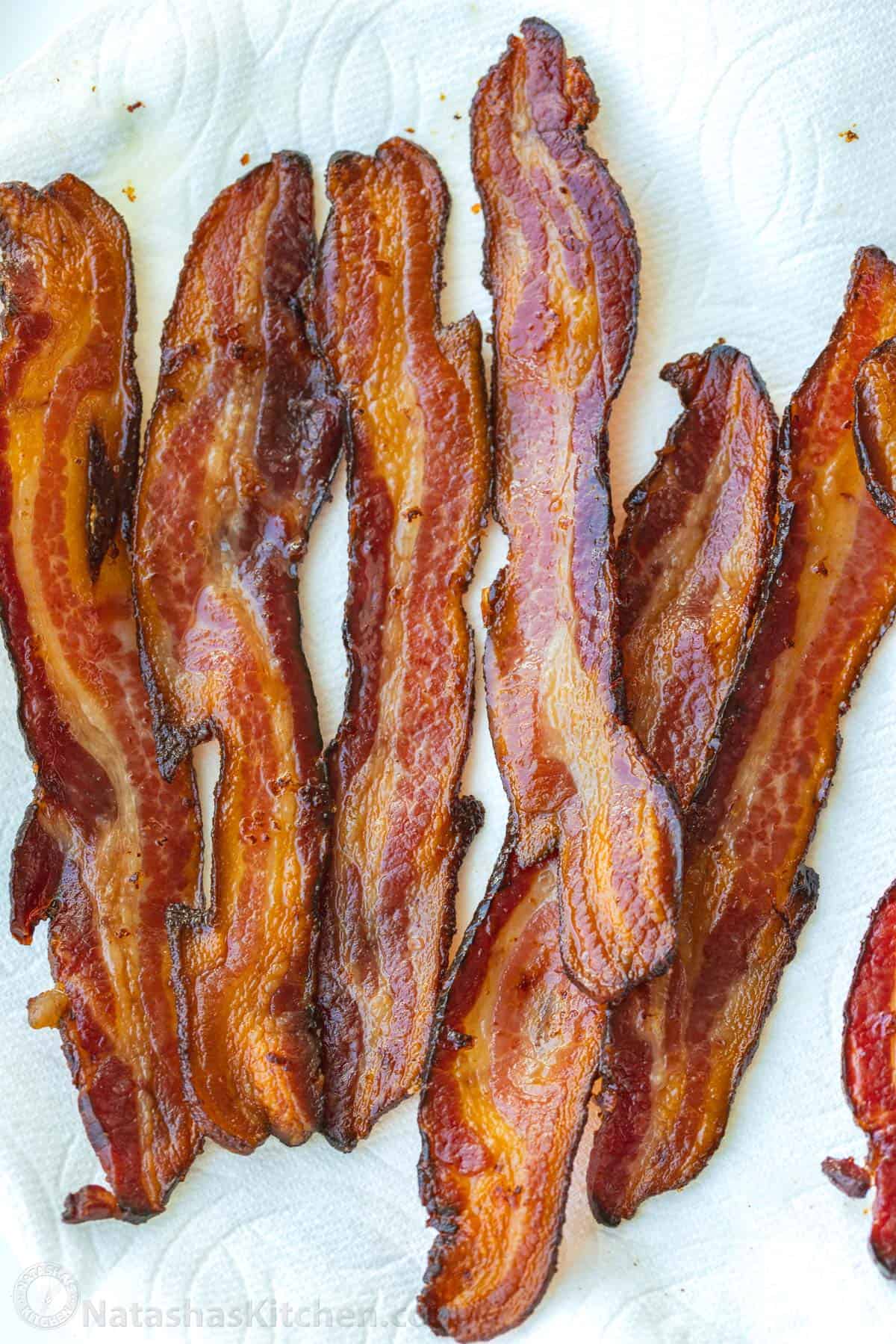 How to bake bacon in the oven that is perfectly crispy. Oven-baked bacon is the best for making a bigger batch and it's the easiest method. Strips of oven-baked bacon on a paper towel