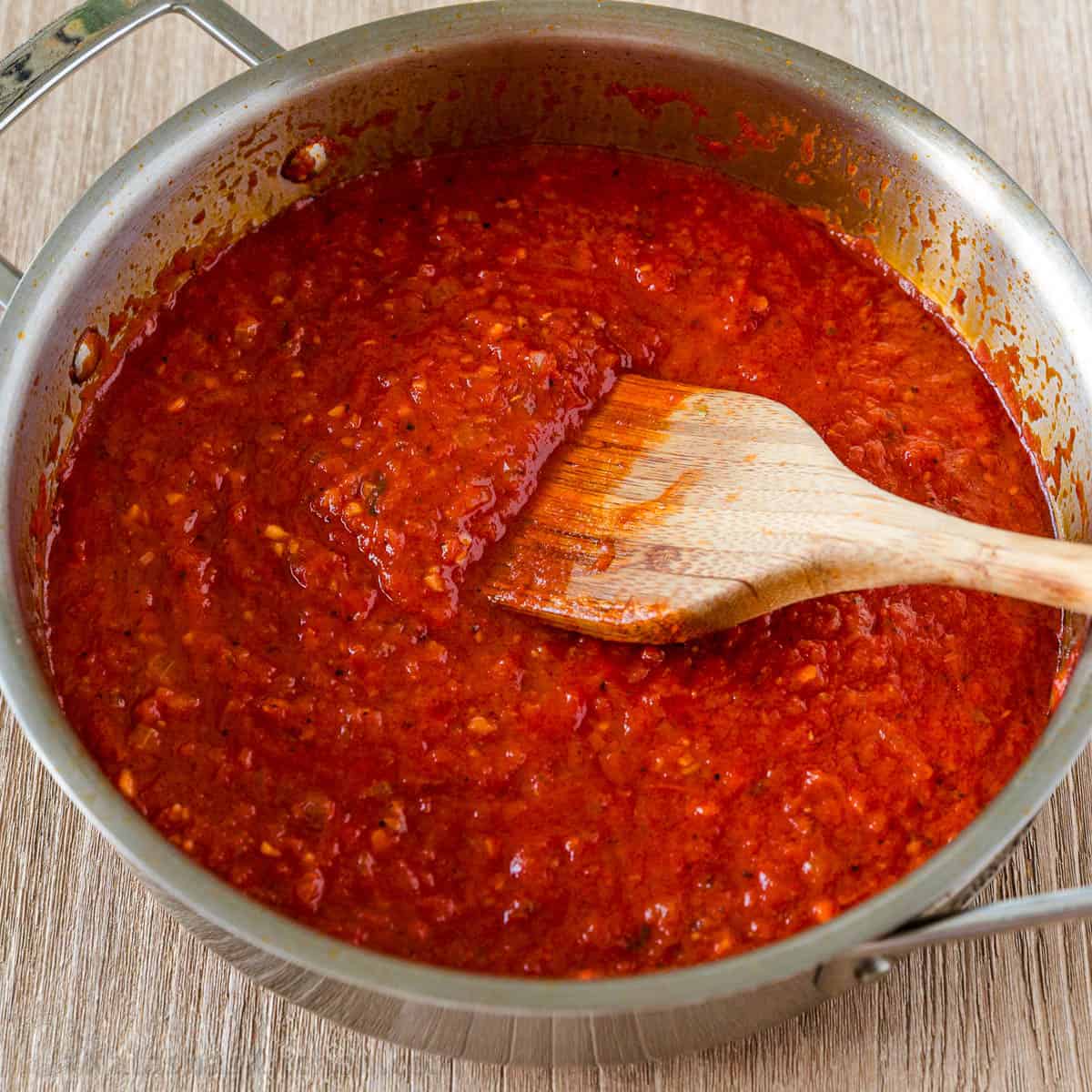 Homemade marinara sauce in a  sauce pan with wooden spoon