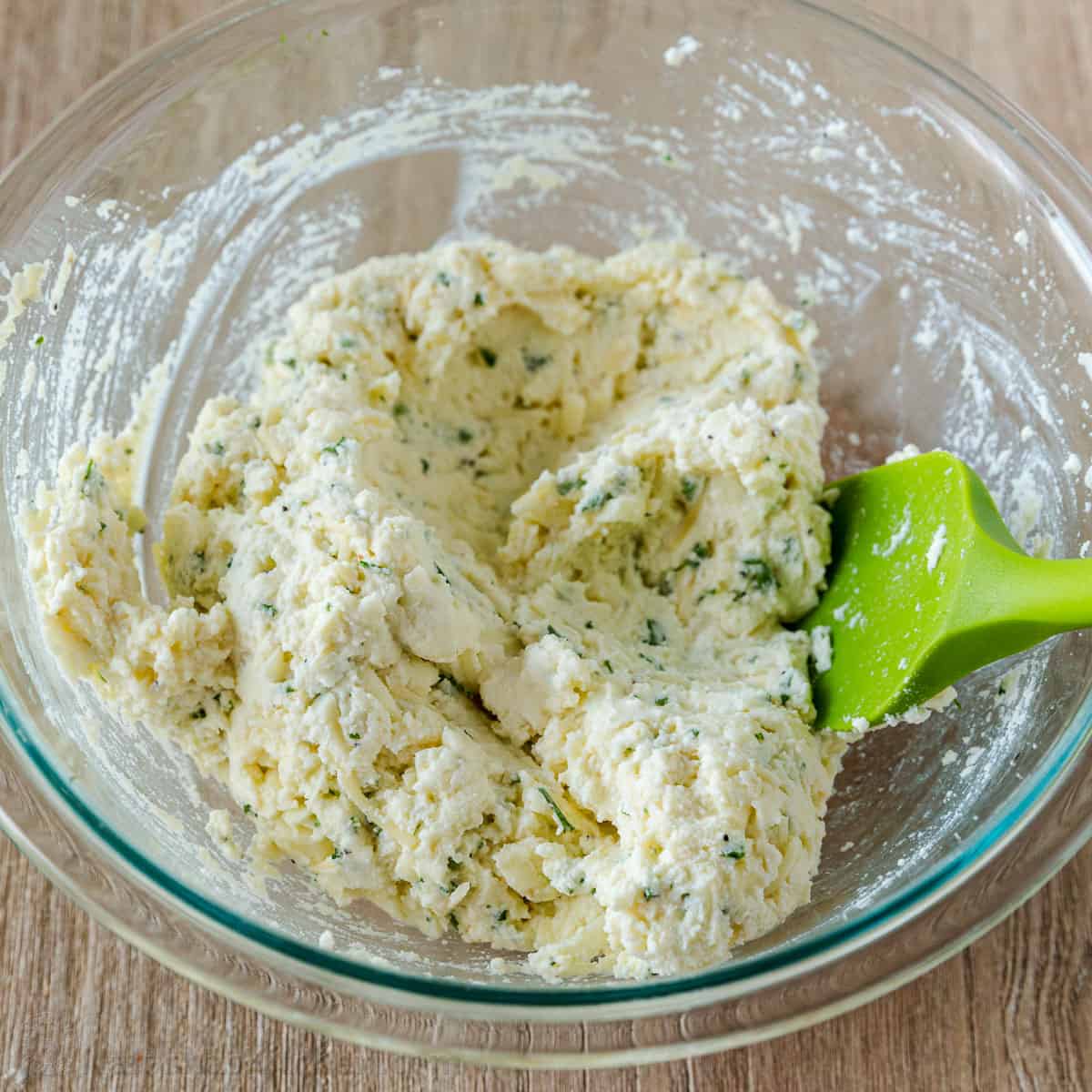 Cheesy filling for stuffed shells in a  clear bowl with green spatula