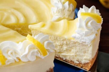 Lemon cheese cake topped with lemon curd and piped whipped cream with one slice being served