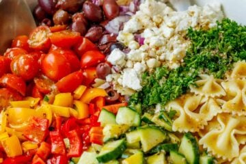 Greek Pasta Salad ingredients being tossed in a white serving dish