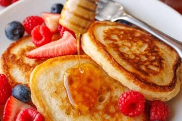 Sourdough discard pancakes stacked on a plate with fresh berries and drizzled honey