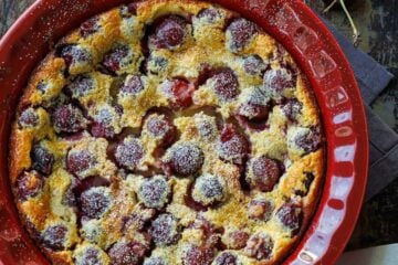 French Cherry clafoutis dessert in a red dish with fresh cherries