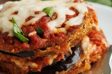 Breaded eggplant Parmesan layered with marinara sauce and mozzarella cheese, and garnished with fresh basil served on a plate with a fork