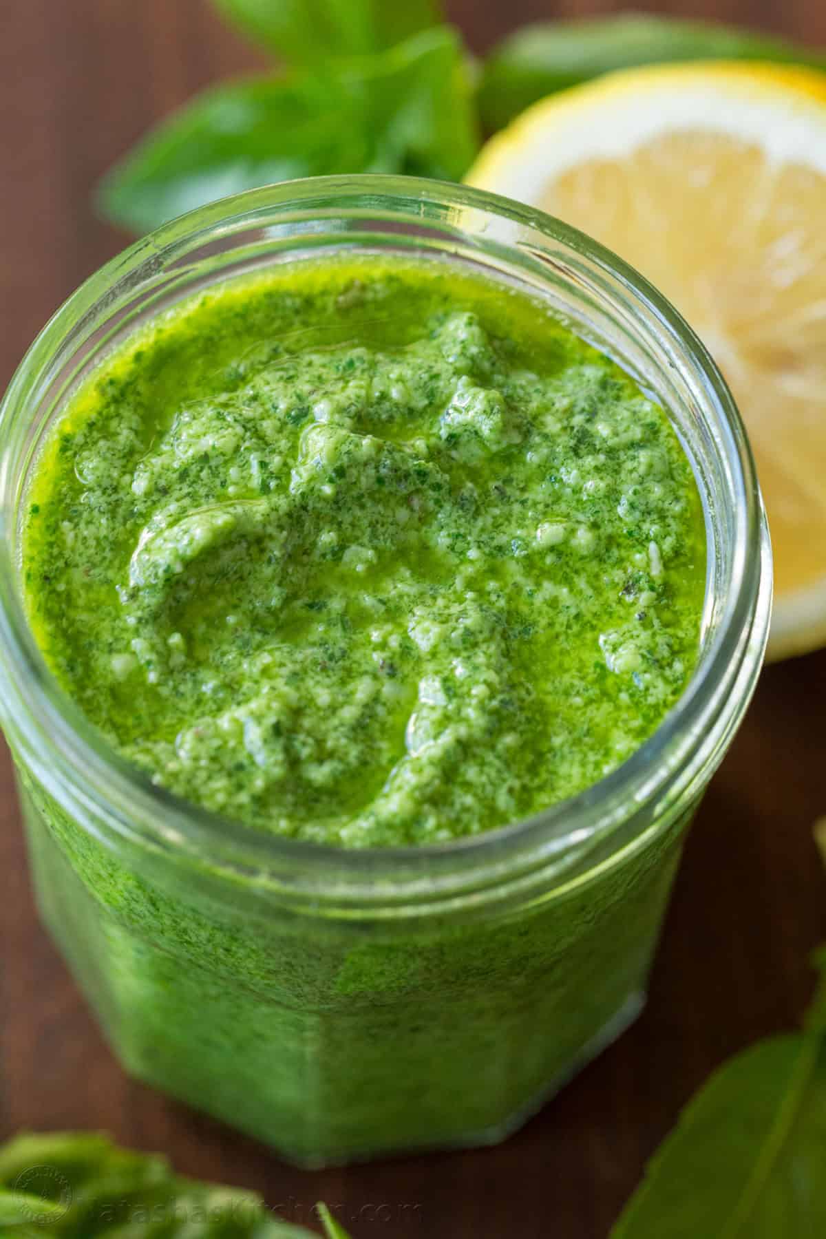 Basil pesto in a mason jar with basil and lemon in background