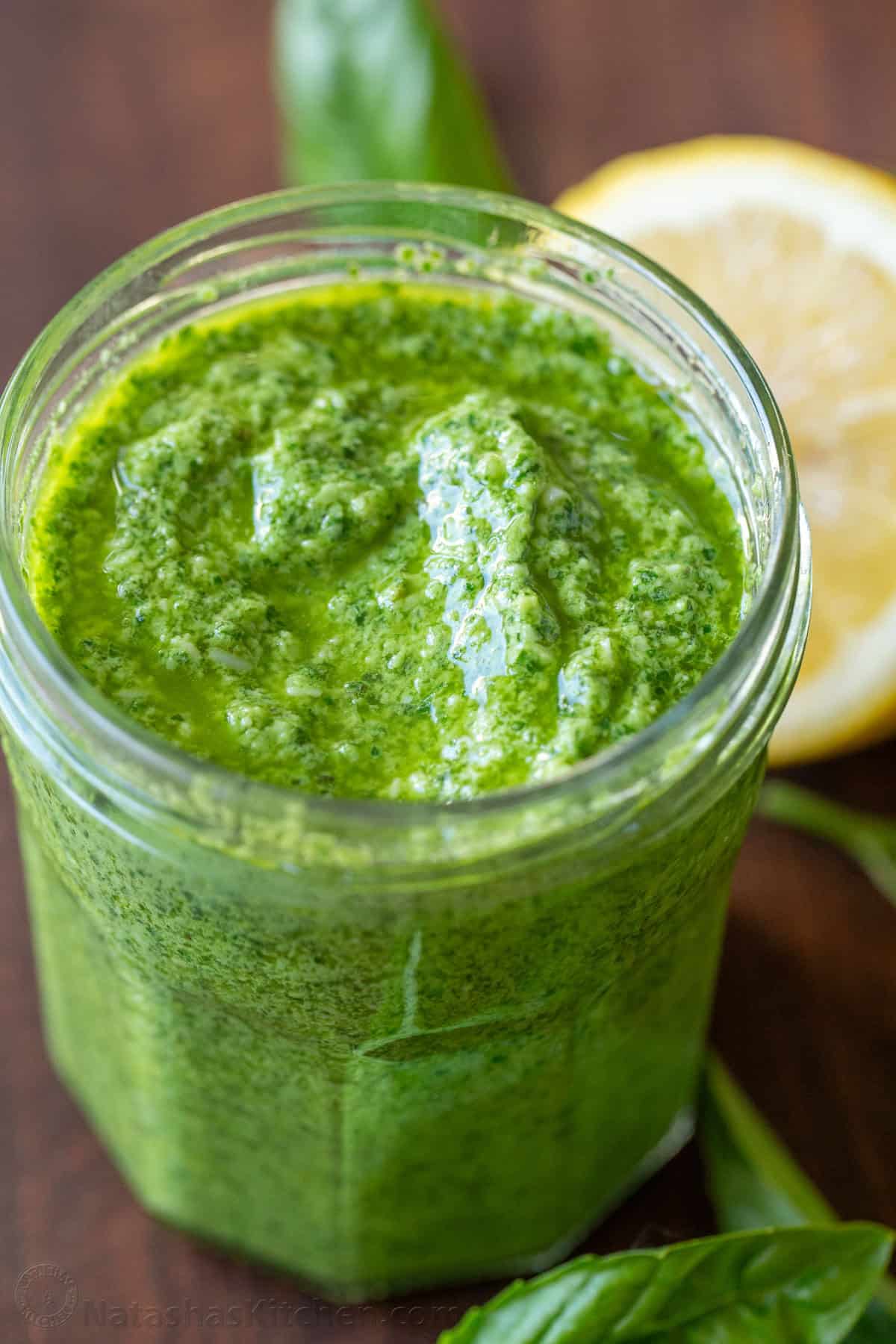 Basil pesto in a mason jar with basil and lemon in background