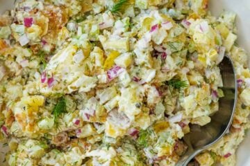 Smashed Potato Salad in a white bowl with a serving spoon, sitting on a red checkered towel.