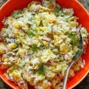Smashed Potato Salad in a red serving bowl with a serving spoon, garnished with fresh dill.