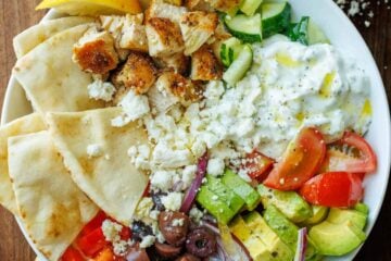 Chopped Greek Chicken Bowl ingredients in a white bowl with lemon wedges and pita bread