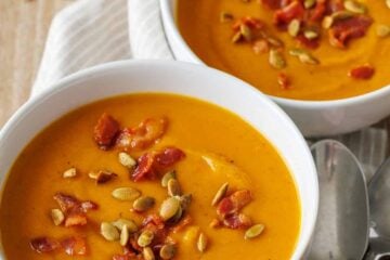 two bowls of pumpkin soup in white bowls with pumpkin seeds and bacon