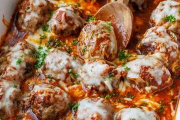 Serving meatball Parmesan using a wooden spoon from a white casserole dish