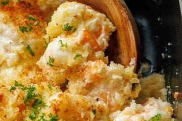 Wooden spoon scooping shrimp casserole out of a dish
