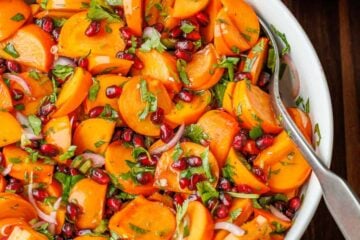 Persimmon pomegranate salad in a white bowl with serving spoon.