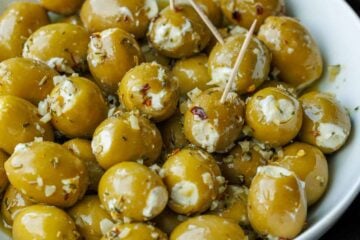 Stuffed green olives with white Boursin cheese, in a white bowl. Some olives have toothpicks for serving.
