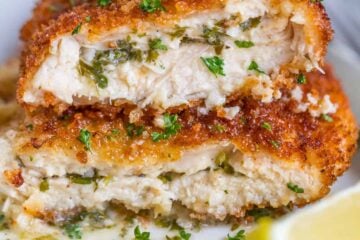 Chicken Kiev recipe cut in half on a white plate with lemon wedge and parsley garnish