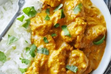 Chicken Korma and white rice in a dish with a fork, garnished with chopped cilantro