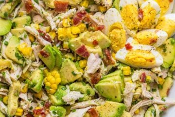 Avocado Chicken Salad in a white bowl with hardboiled eggs and bacon bits on top