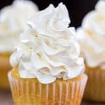 Vanilla buttercream frosting on a yellow cupcake with more cupcakes behind